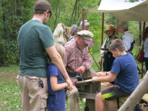 Steve B helping guests use a draw knife and a shaving horse to create a canoe paddle.